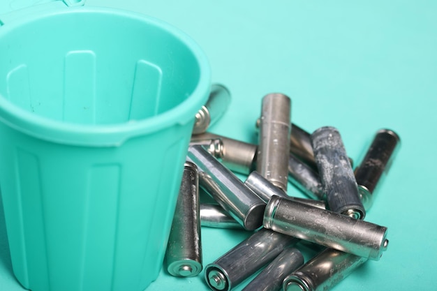 Baterías de dedos usadas cerca de un contenedor de basura en miniatura Fondo verde claro Primer plano