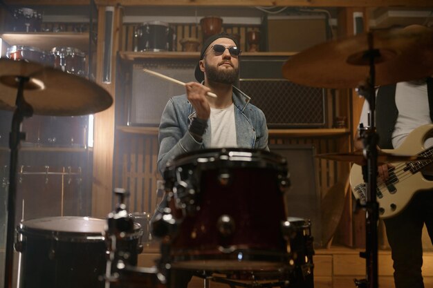 Foto baterista elegante tocando música na bateria durante a apresentação de uma banda de rock em um clube de concerto de rock