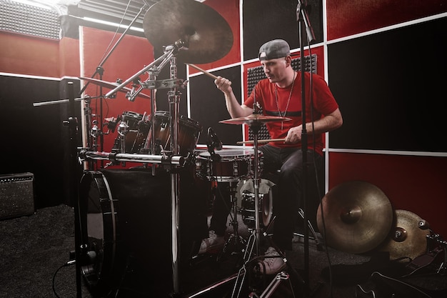 El baterista profesional moderno toca la batería en una base de ensayo, estudio de grabación rojo y negro