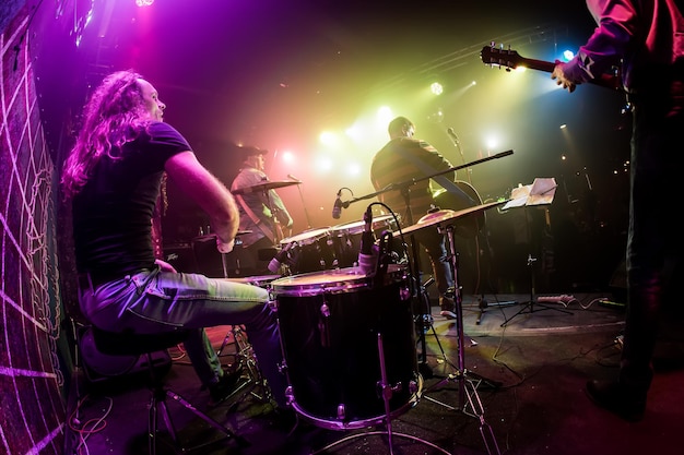 El baterista tocando la batería en el escenario. Advertencia: concéntrese en el tambor, disparos auténticos con iso alto en condiciones de iluminación desafiantes. Un poco de grano y efectos de movimiento borrosos.