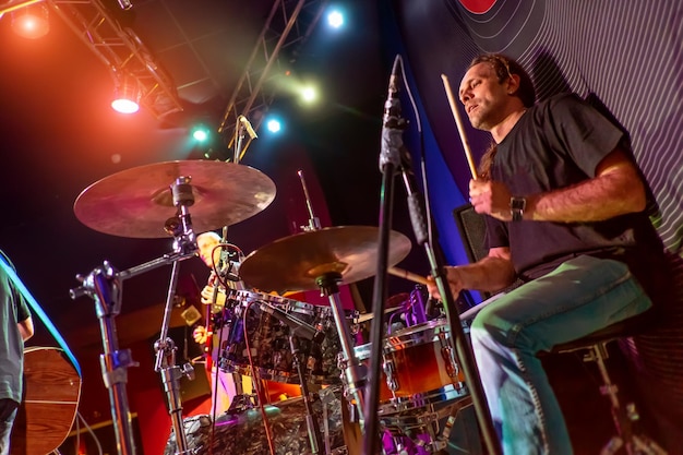 Baterista tocando bateria no palco. Disparo autêntico com alto iso em condições de iluminação desafiadoras. Um pouco de grão e efeitos de movimento borrado.