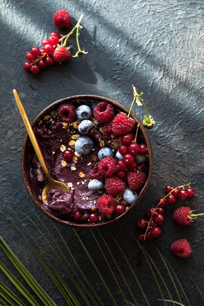 Batido de acai congelado en cáscara de coco con frambuesas, plátano, arándanos, frutas y granola sobre fondo de hormigón. Desayuno, comida saludable para las vibraciones del verano, vista superior, espacio para texto