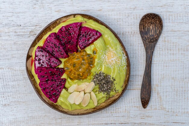 Batido de aguacate verde en tazón de coco con fruta del dragón, maracuyá, hojuelas de almendras, chips de coco