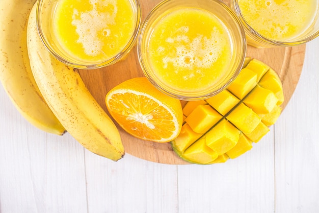 Batido amarillo de mango, plátano y naranja sobre una mesa de madera blanca.