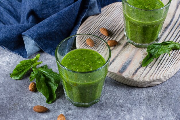 Batido de batido verde con manzana verde, espinaca, kiwi y almendras sobre fondo de concreto gris.