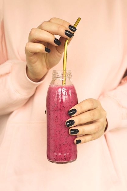 Batido de bayas en una botella. Desayuno saludable en manos de una mujer.