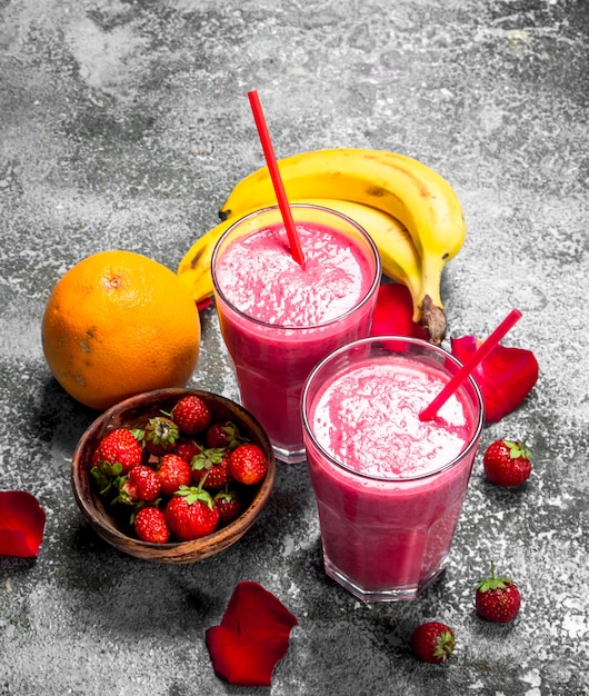 Foto batido de bayas con plátano y pétalos de rosa sobre fondo rústico