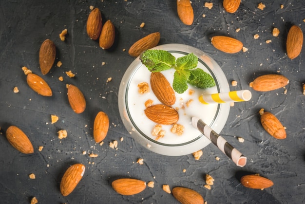 Batido blanco hecho de yogur, plátano y nueces almendras decorado con menta sobre una mesa de hormigón oscuro