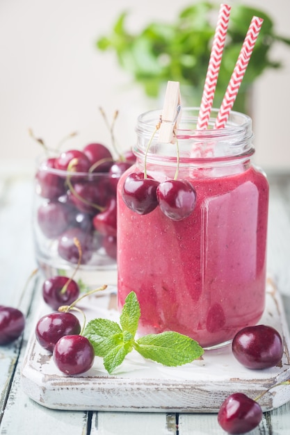 Batido de cereza saludable con fresa congelada, agua de coco y miel en vidrio sobre mesa de madera blanca.