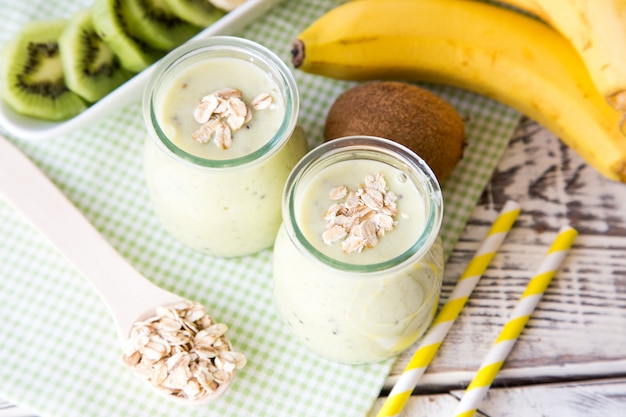 Batido de banana com kiwi e aveia em uma mesa de madeira clara.