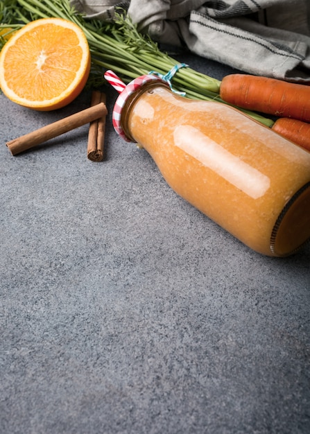 Batido de cenoura saudável com laranja e canela na garrafa de vidro e ingredientes.