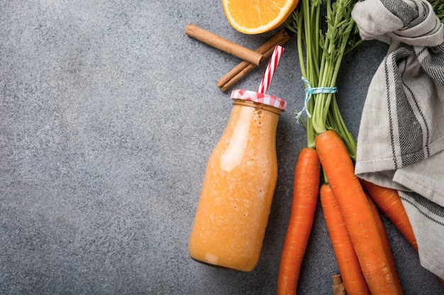 Batido de cenoura saudável com laranja e canela na garrafa de vidro e ingredientes.