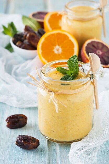 Batido de fruta saudável e fresco de laranja e tâmara na mesa de madeira azul. Foco seletivo.