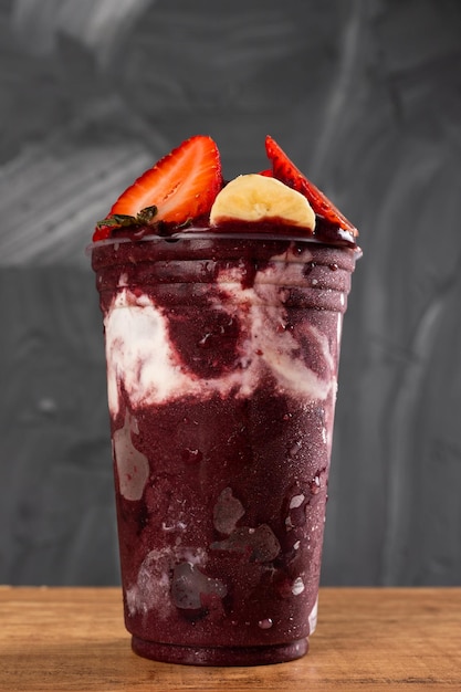 Batido de sorvete brasileiro frozen aã§ai berry em copo plã¡stico com morangos, bananas e leite condensado. no fundo cinza do verão. vista frontal para menu e mídia social