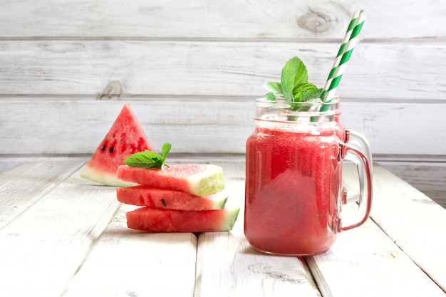 Batido de desintoxicación refrescante de verano de sandía y menta sobre un fondo blanco de madera.