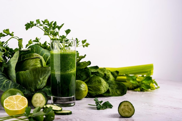 Batido de desintoxicación de vegetales verdes en vidrio en fondo blanco de madera.