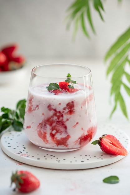 Batido de fresa casero, cóctel en un vaso con fresas frescas en una pared gris con hojas verdes. concepto de comida vegana.