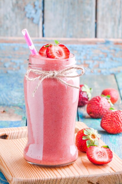 Batido de fresa en un frasco con una pajita sobre una mesa de madera