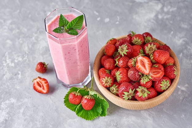 Batido de fresa en frasco de vidrio y fresas frescas en un tazón de madera sobre un fondo gris. Desayuno saludable