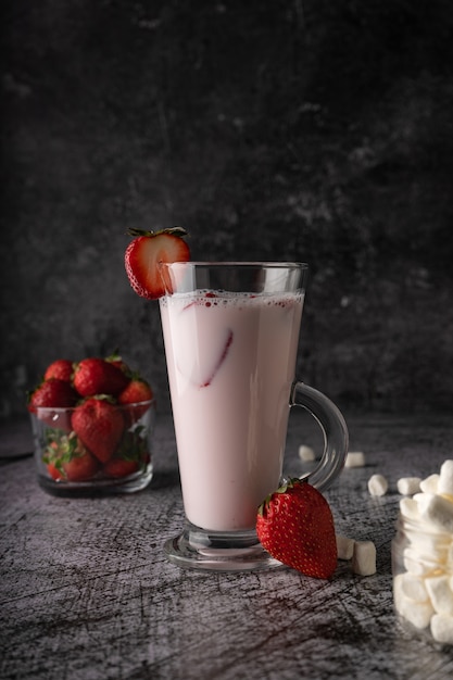 Un batido de fresa con leche de bebida fría con fresas frescas y nata en un vaso transparente alto