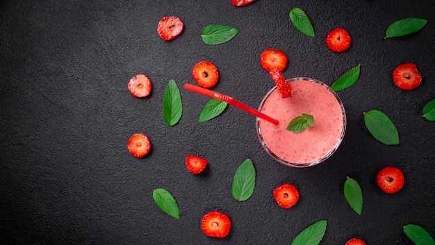 Batido de fresa con menta en un vaso sobre un fondo de piedra oscura. Alimentación saludable para desayunos y meriendas. Endecha plana. Vista superior