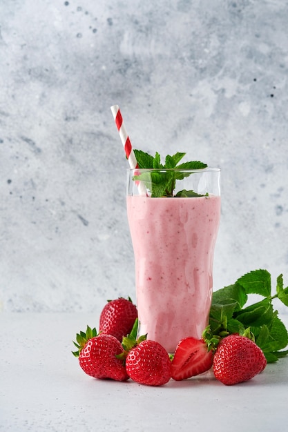 Foto batido de fresa o batido con bayas y menta en vaso alto sobre fondo gris claro. bebida de verano concepto orgánico de batido, batido y refresco. lugar para el texto.