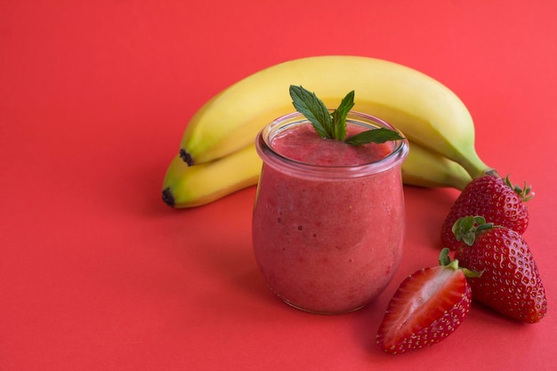 Batido con fresa y plátano en el frasco de vidrio sobre el fondo rojo Espacio de copia Primer plano