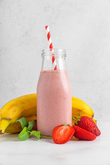 Batido de fresa y plátano fresco en una botella de vidrio con paja y menta sobre fondo blanco Orientación vertical