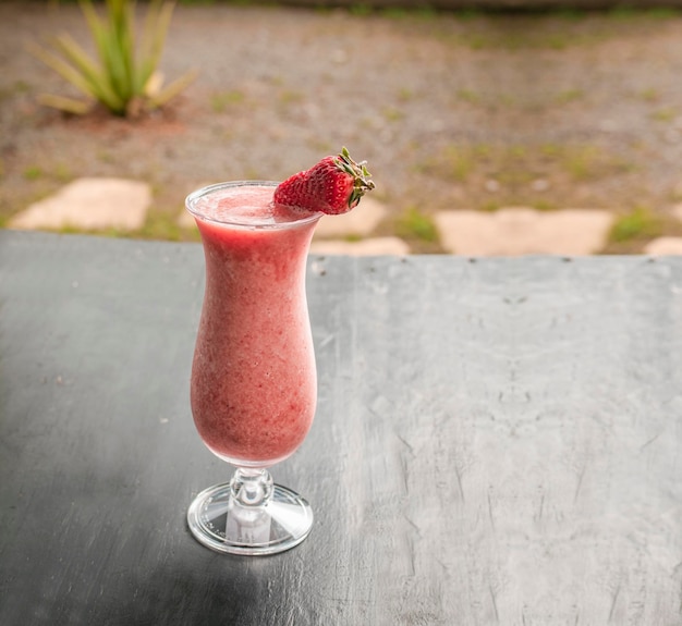 Batido de fresa saludable en vidrio sobre madera oscura Batido de fresa en madera oscura con fondo borroso Primer plano Delicioso batido de fresa con trozos de fresa en madera