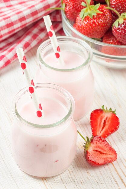 Batido de fresa en el tarro de cristal con pajita sobre mesa de madera blanca