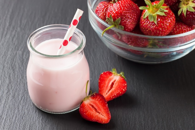 Batido de fresa en el tarro de cristal con pajita sobre superficie de pizarra negra.