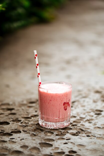 Batido de fresa en un vaso con una pajita en la piedra