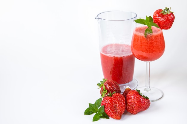 Batido de fresa en un vaso sobre una pierna alta decorado con fresas y menta en blanco