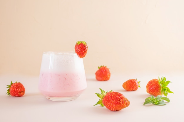 Batido de fresa en un vaso transparente. Alrededor - fresas. El concepto de deliciosas bebidas frescas, alimentos saludables para el desayuno y la merienda.