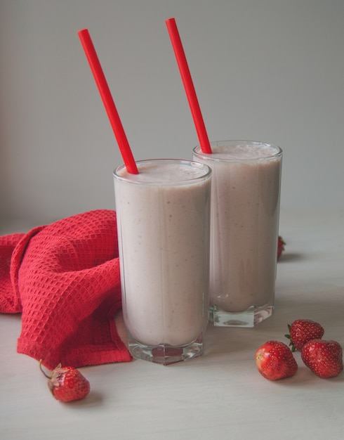 Batido de fresa de verano en vasos con pajitas de color rojo brillante sobre un fondo de madera blanca Bebida de verano