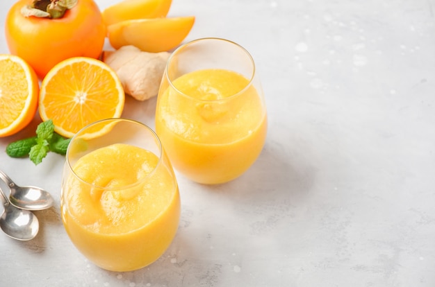 Batido fresco y saludable con caqui, naranja y jengibre sobre concreto gris