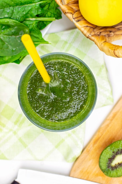 Foto batido con hojas frescas de espinaca, manzana y kiwi en vaso con pajita, vista superior vertical.