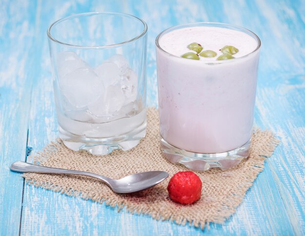 Foto batido de leche con fresas, grosellas y hielo sobre una mesa azul.