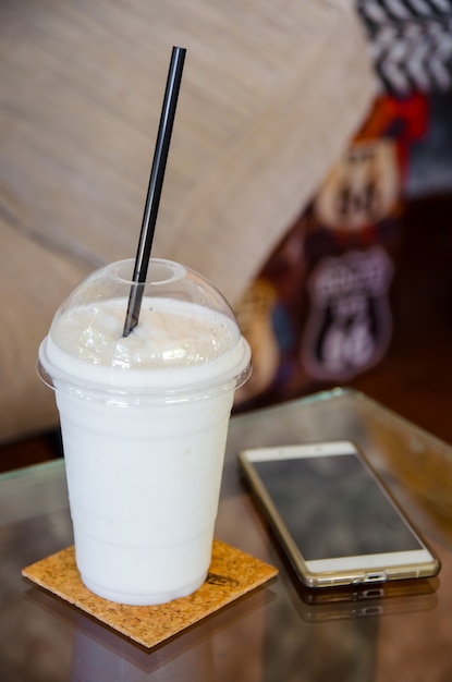 Batido de leche con smartphone en mesa de cristal.