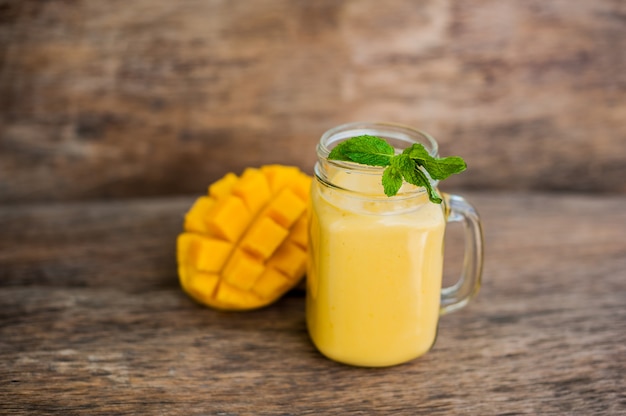 Foto batido de mango en un vaso mason jarra y mango en el fondo de madera vieja. batido de mango.