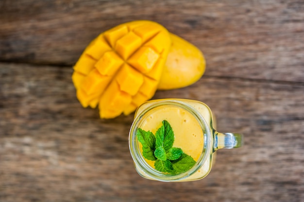 Foto batido de mango en un vaso mason jarra y mango en el fondo de madera vieja. batido de mango.