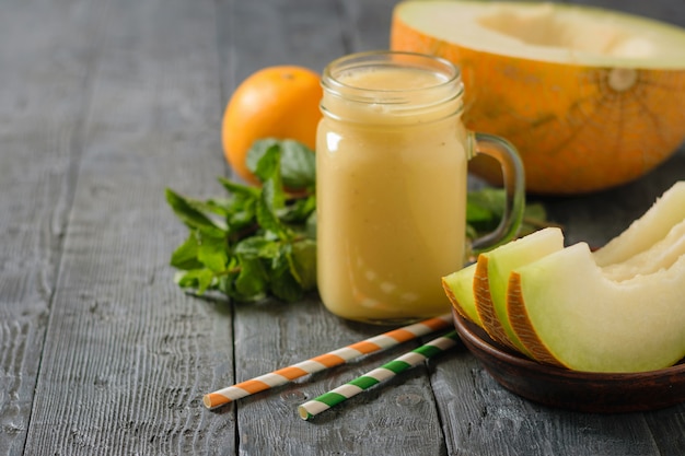 Batido de melón, tubos de cóctel amarillos y verdes y rodajas de melón fresco sobre una mesa de madera