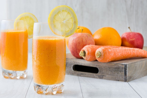 Batido de naranja, manzana y zanahoria en mesa de madera blanca