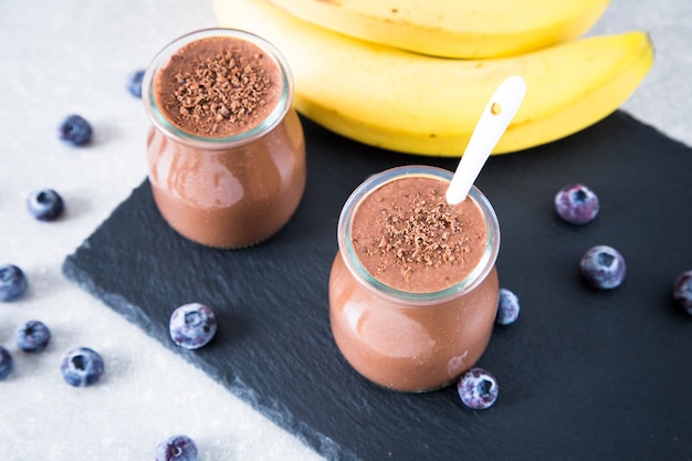 Batido de plátano y chocolate con semillas de chia y arándanos sobre un fondo de pizarra y piedra.