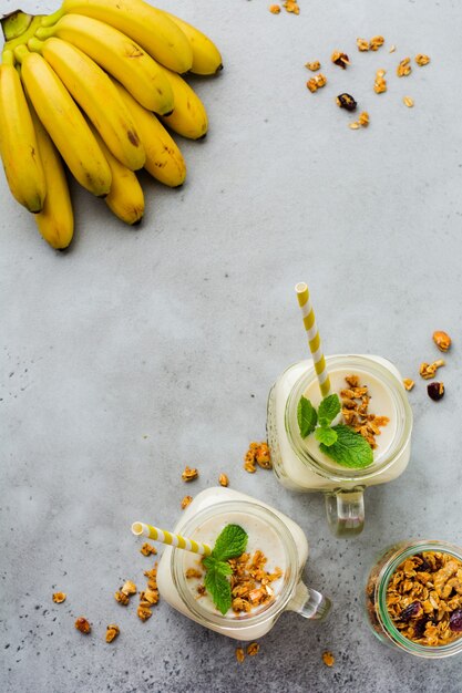 Batido de plátano con granola, frutos secos y menta sobre superficie de hormigón gris