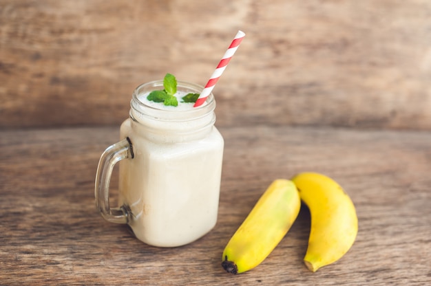 Batido de plátano y plátanos frescos sobre un fondo de madera