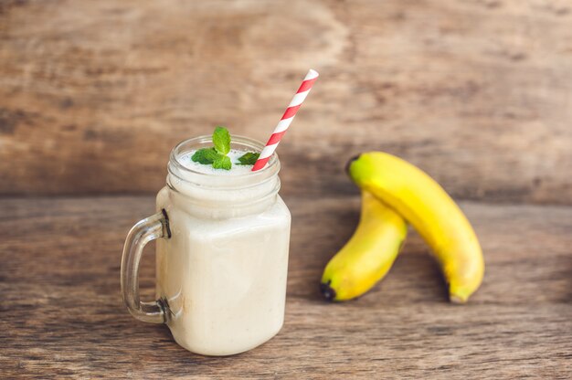 Batido de plátano y plátanos frescos sobre un fondo de madera