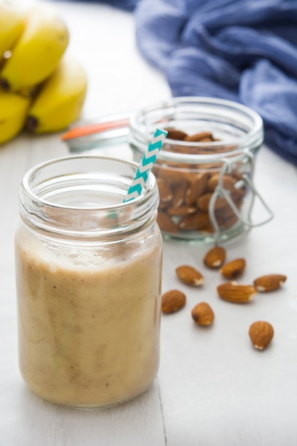 Batido de plátano saludable con almendras en vidrio en mesa de madera blanca