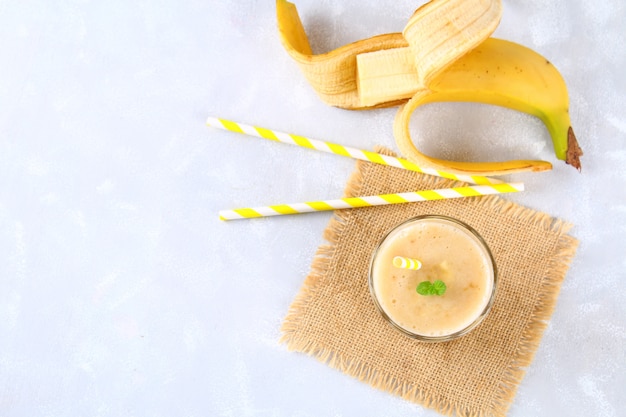 Batido de plátano con tubo de papel y menta. Los plátanos son enteros y cortados sobre un fondo gris.