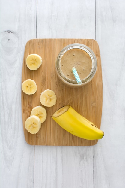 Batido de plátano en una vista de mesa de madera blanca